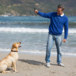 smiling man playing with dog on the beach.