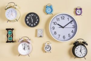 9 wall clocks and 1 sand timer arranged on a wall.