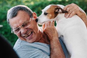 Man laughing and getting licked by his dog on the cheek.